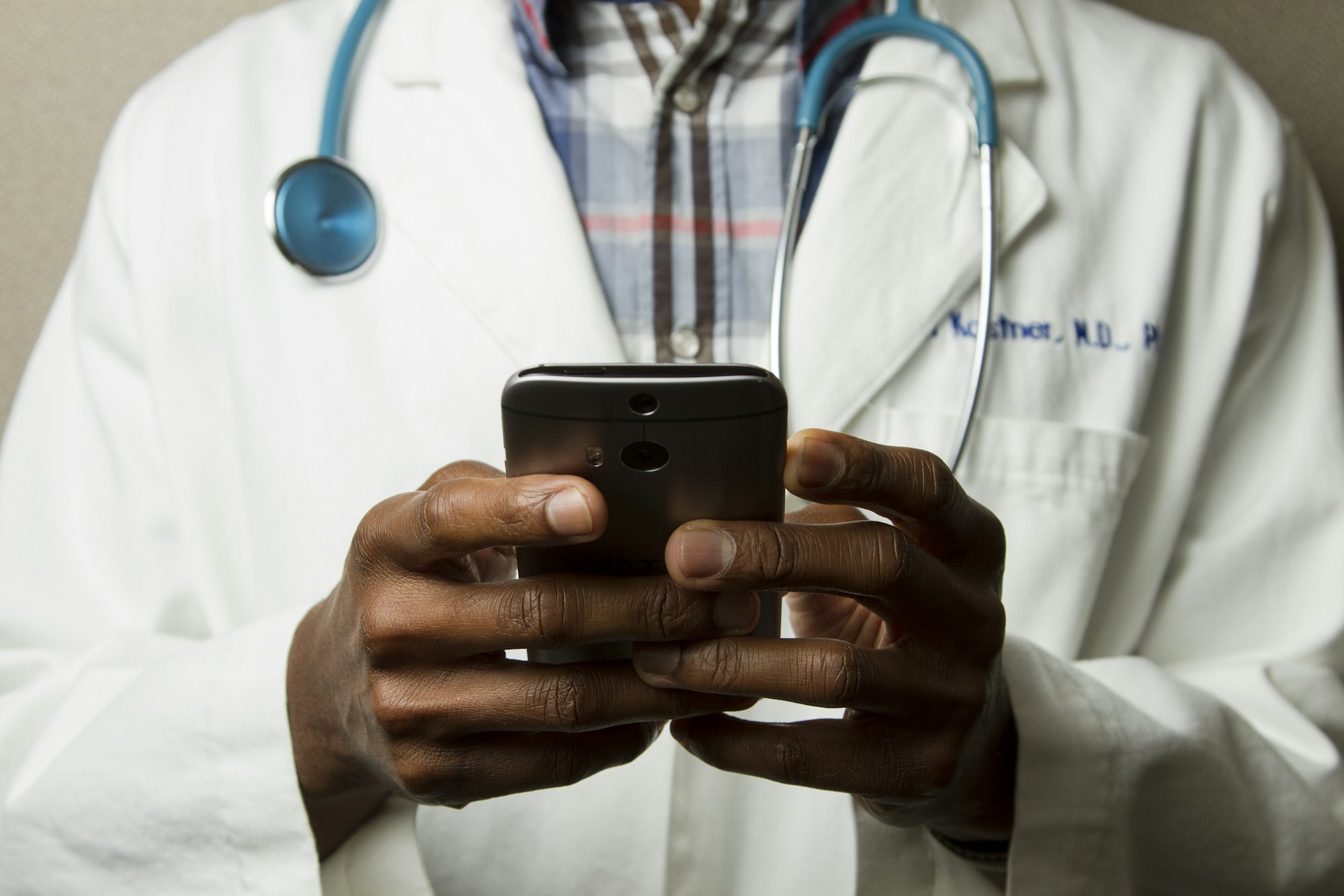 A doctor in a white coat holding a smartphone, a stethoscope around the neck