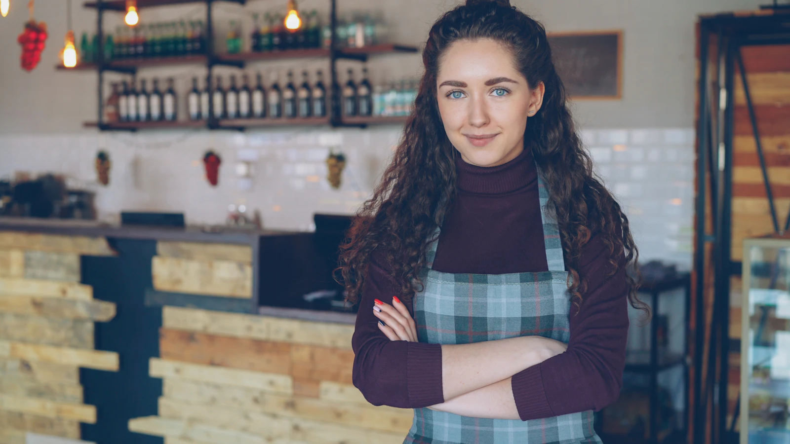 A smiling coffee shop owner standing at her counter with her arms crossed