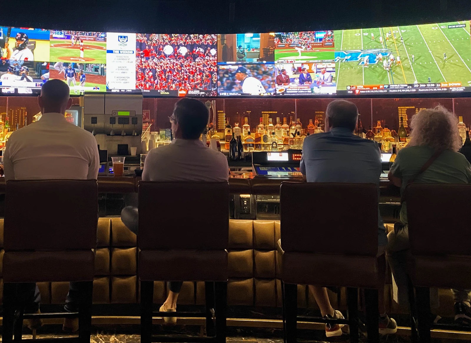 Guests sitting at a bar watching a game on a wall of TVs