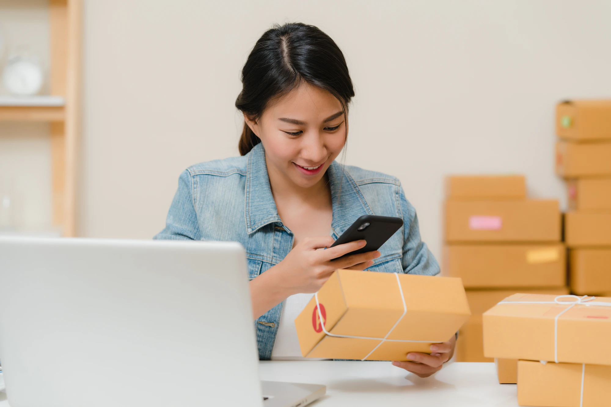 A shop owner smiling at a customer text on her phone, with packed orders beside her