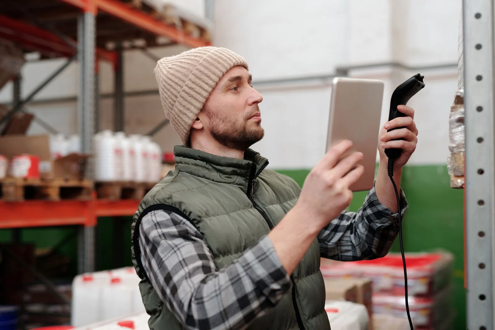 A warehouse worker holding a tablet and a barcode scanner beside the racking