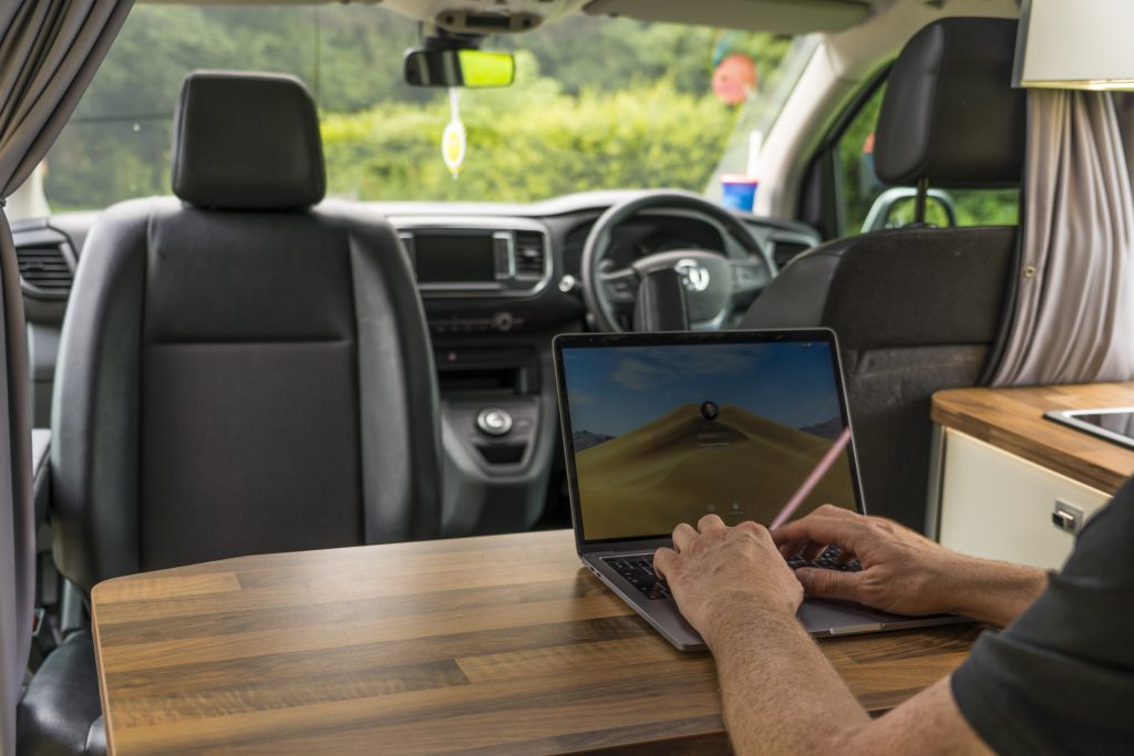 A laptop on the table of a camper van, hills outside the window