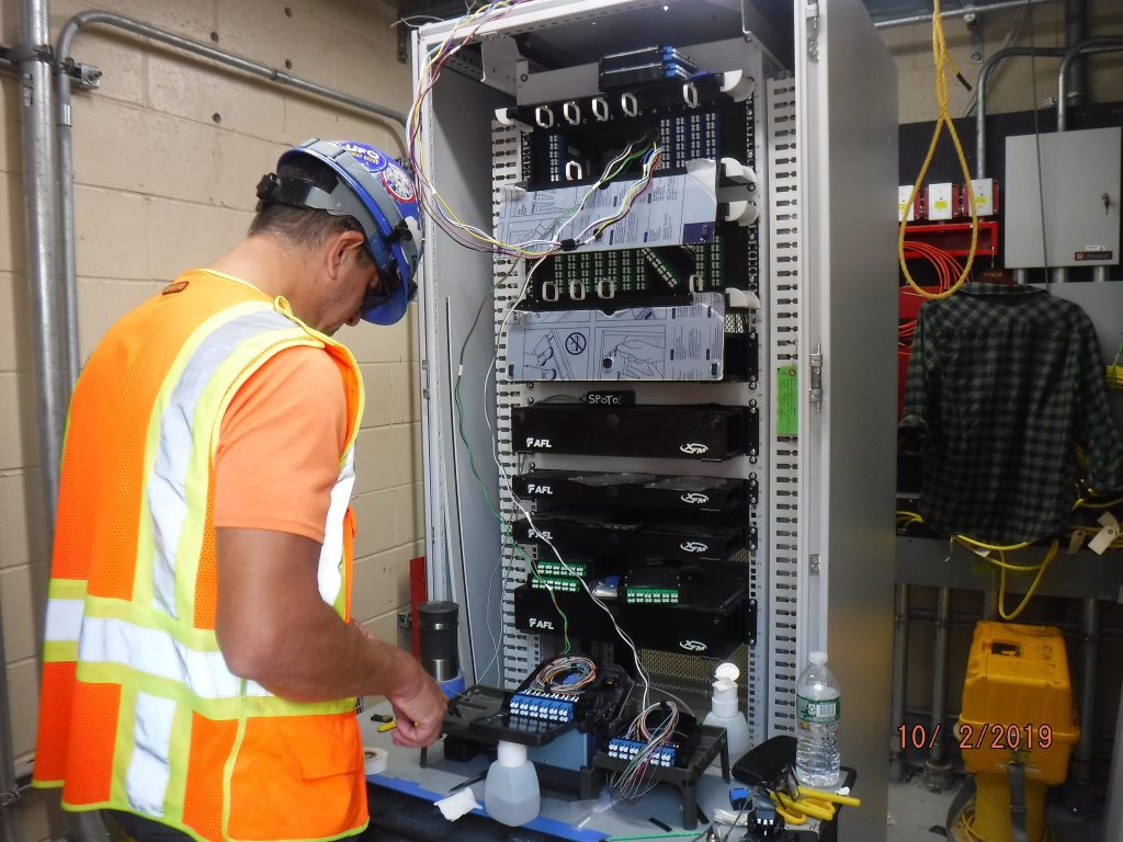 Technician in a safety vest splicing fibre in a cabinet