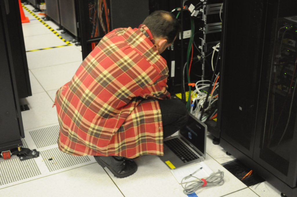 Technician with a laptop working at the base of a server rack