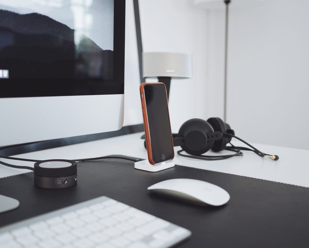 A tidy black and white computer desk with a phone, headphones and a mouse