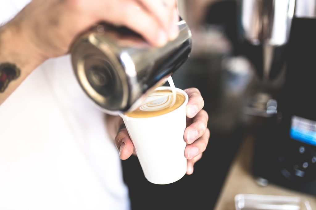 A barista pouring steamed milk into a takeaway coffee cup