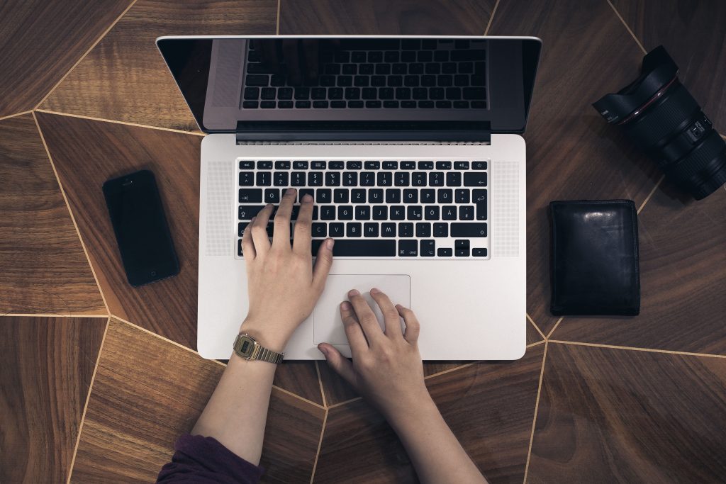 Hands on a laptop keyboard beside a phone and a wallet