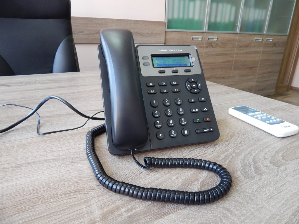 A black desk phone with a corded handset on a wooden desk