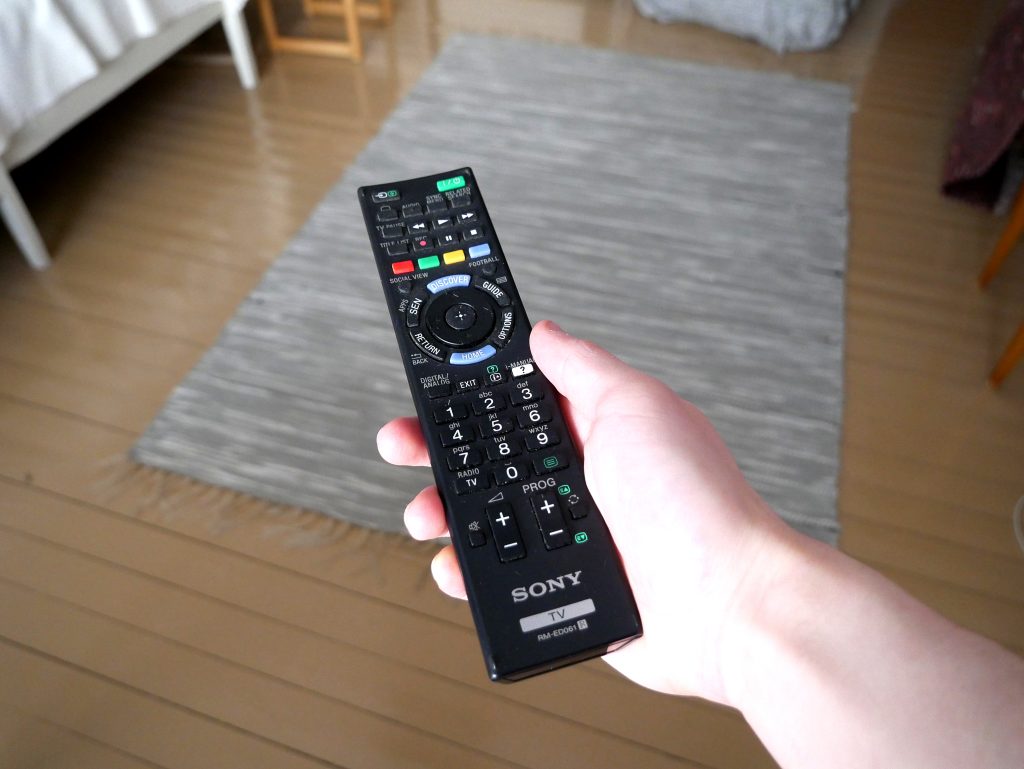 A hand holding a TV remote control in a living room