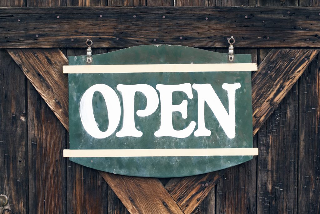 A wooden Open sign hanging on a shop's slatted wall