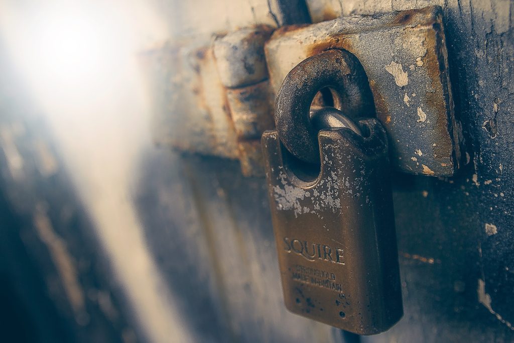 A rusty padlock on a weathered teal gate