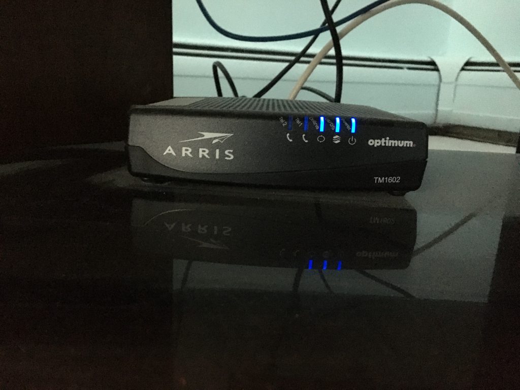 A black cable modem with blue status lights in a dark room