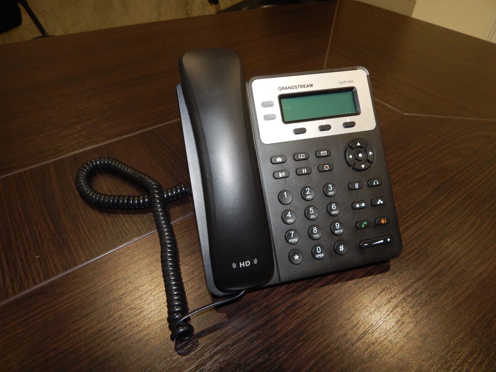 A black desk phone with its handset on a wooden desk
