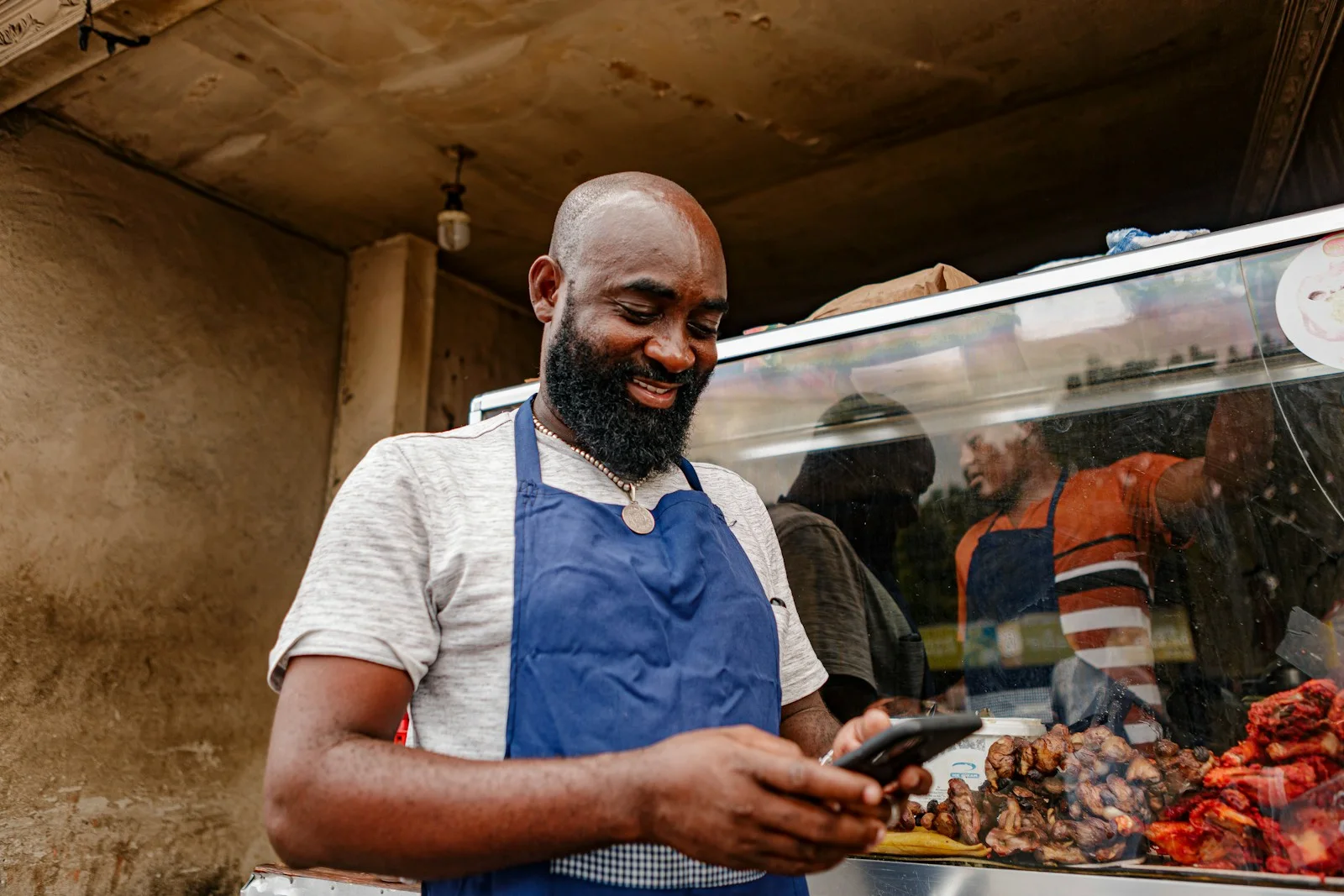 A shop owner in an apron smiling at his phone at his counter